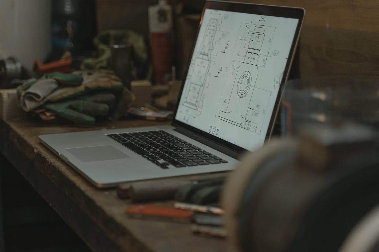 Laptop z rysunkiem technicznym CAD otwartym na warsztacie metalowym